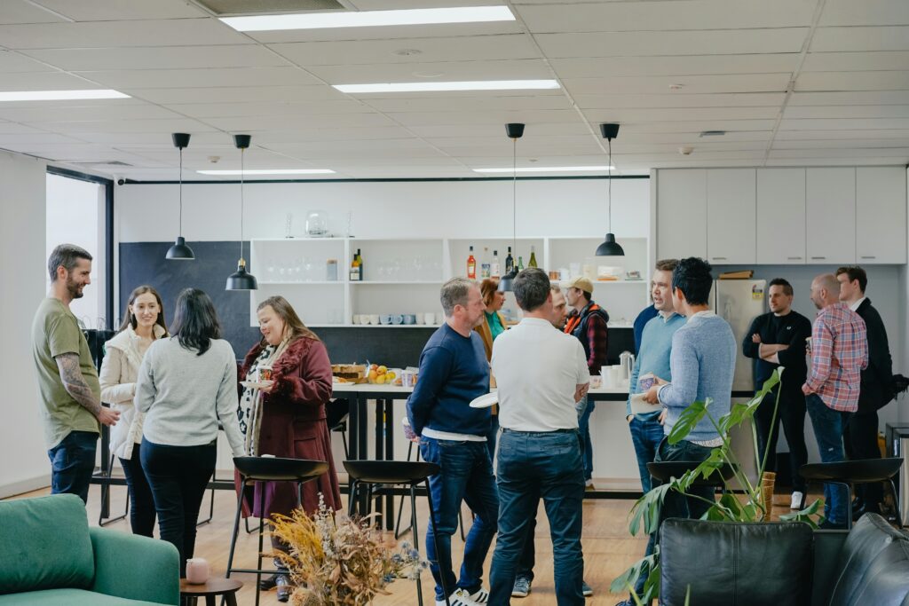 A group of people socialising and conversing in a modern office kitchen area.